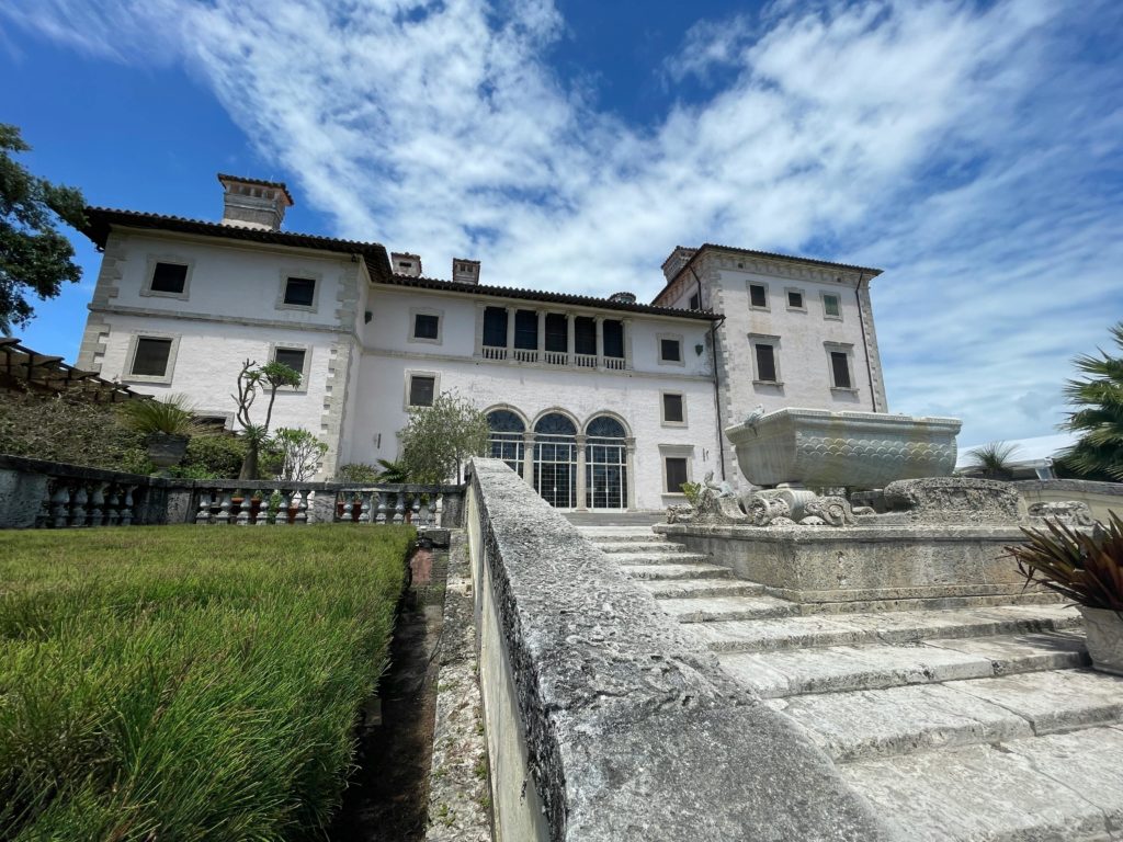 Beautiful facade of a historic mansion with a stunning stone fountain under a clear blue sky.