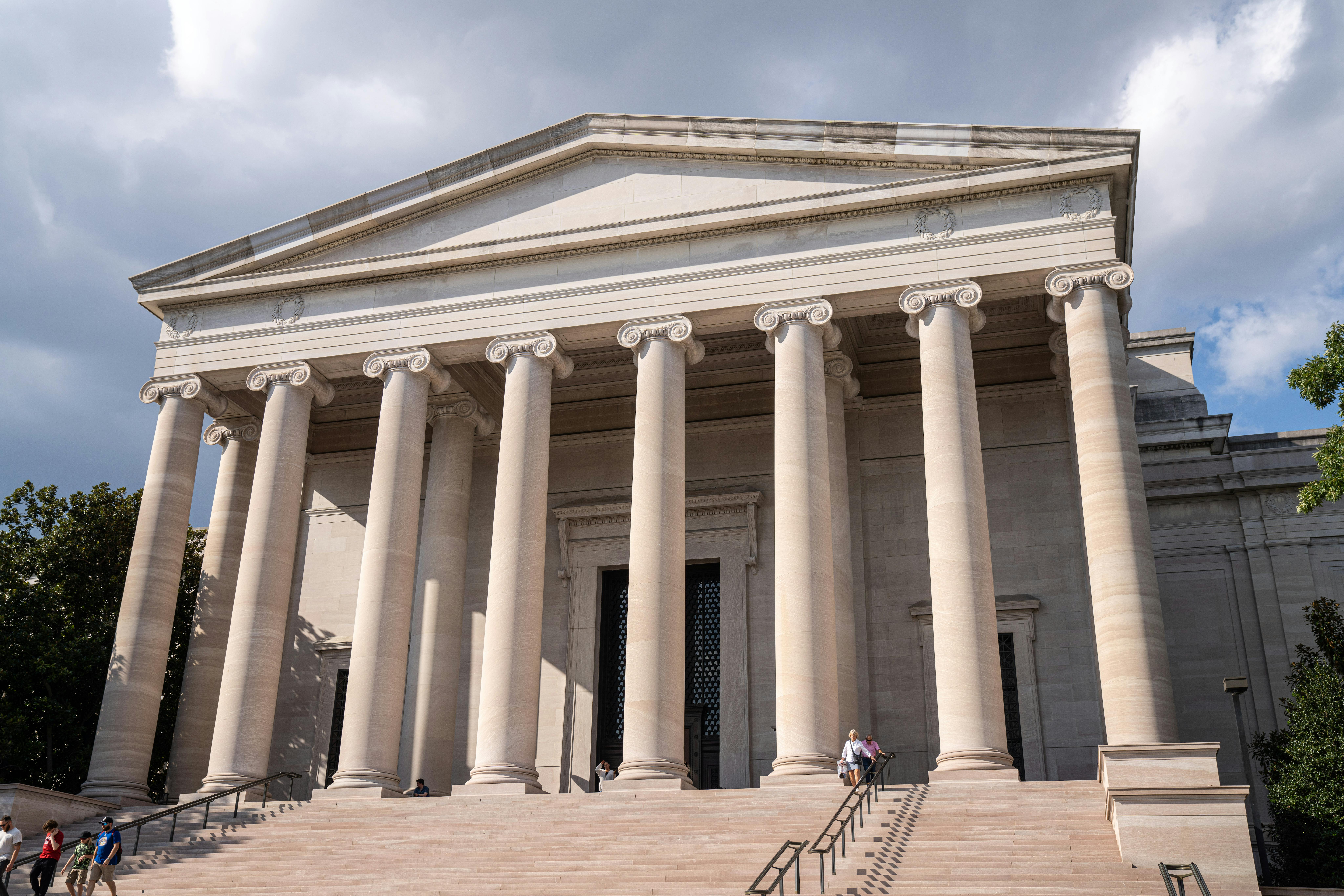 Grand neoclassical building with towering columns under a cloudy sky.