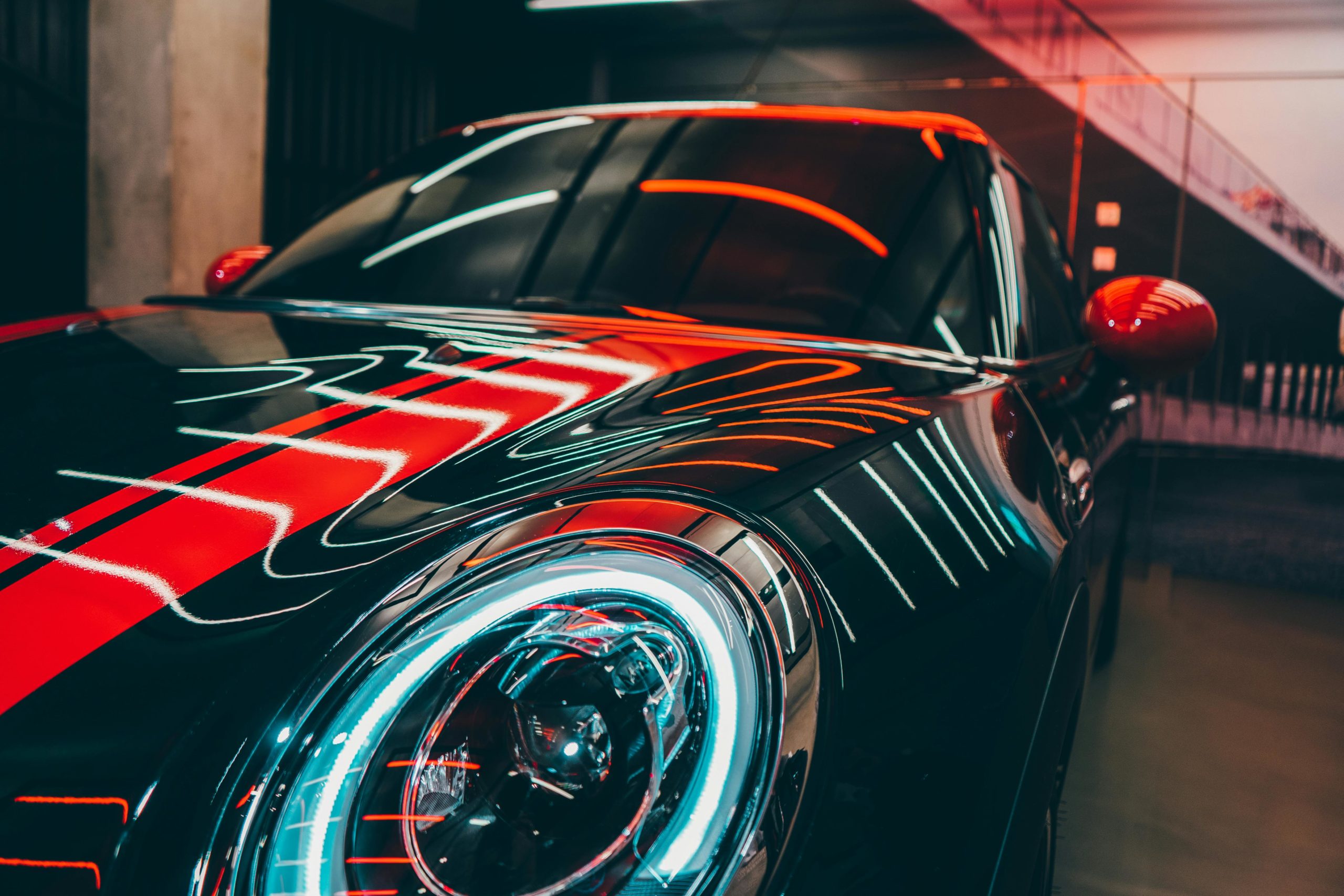 A luxury sports car in a modern setting with vibrant red and neon lights reflecting on the surface.